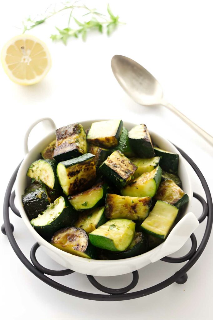 Bowl of sauteed zucchini and fresh herbs nearby.
