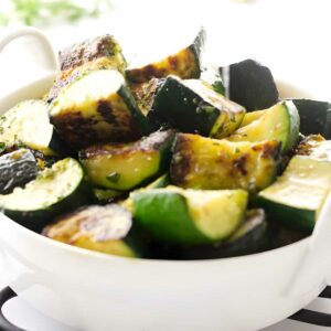 Hand squeezing lemon over sauteed zucchini slices.