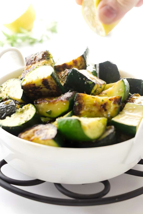 Hand squeezing lemon over sauteed zucchini slices.