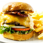 A bacon cheeseburger on a plate with French fries.