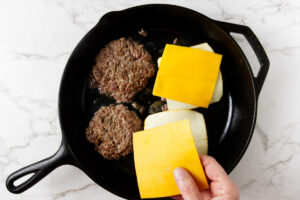 Topping beef patties with cheese in a skillet.