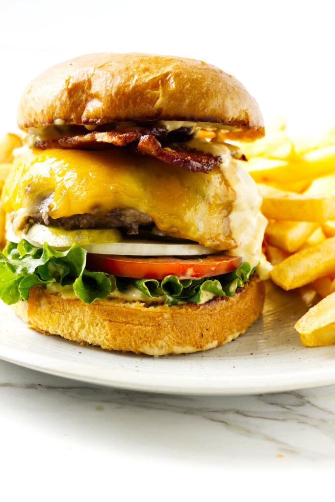 A bacon cheese burger on a plate with French fries.