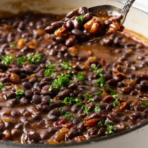 A spoon scooping barbecue black beans from a pot.