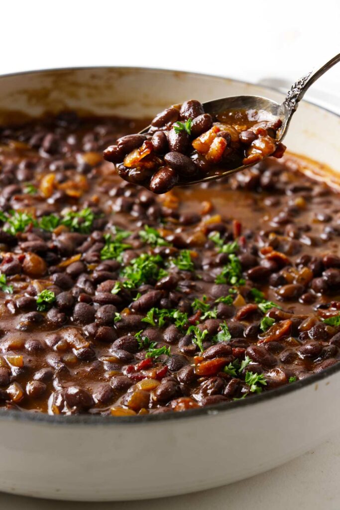 A spoon scooping barbecue black beans from a pot.