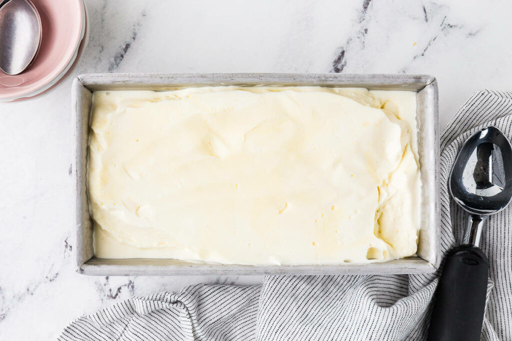 Vanilla custard ice cream in a metal pan next to an ice cream scooper.