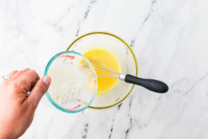 Pouring hot milk into the egg yolk mixture to make custard for ice cream.