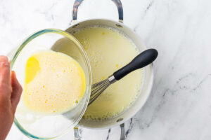 Pouring the tempered egg yolks into the pot of hot milk.