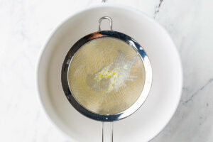 Pouring ice cream custard through a strainer into a bowl.