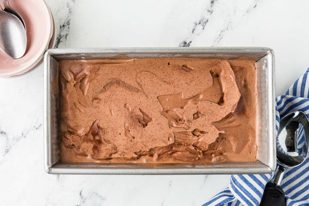 Rectangular pan of chocolate ice cream with scooper and bowls nearby.