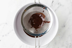Pouring chocolate ice cream custard through a strainer.