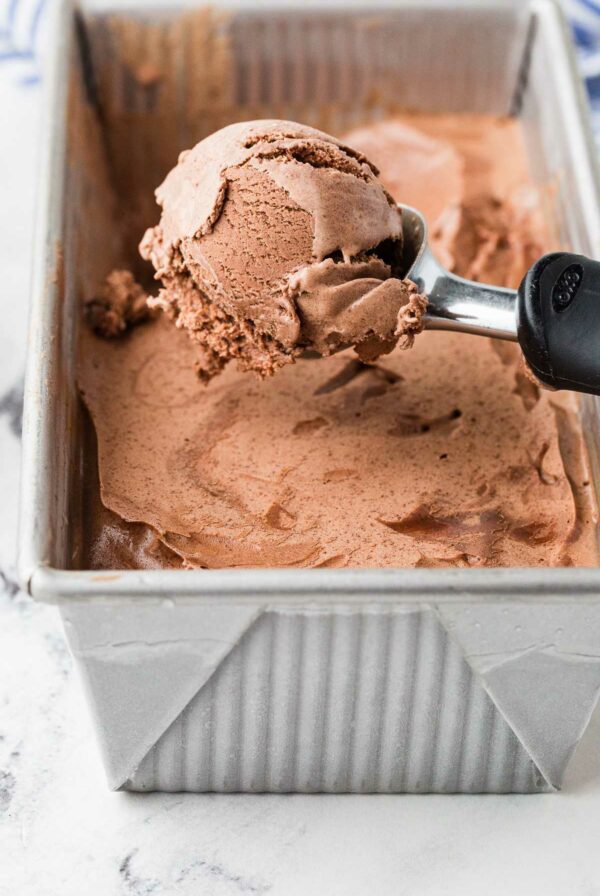 Scooping chocolate ice cream out of a pan.