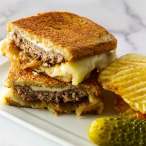 A beef and cheese patty melt sandwich with sautéed onions on a plate.