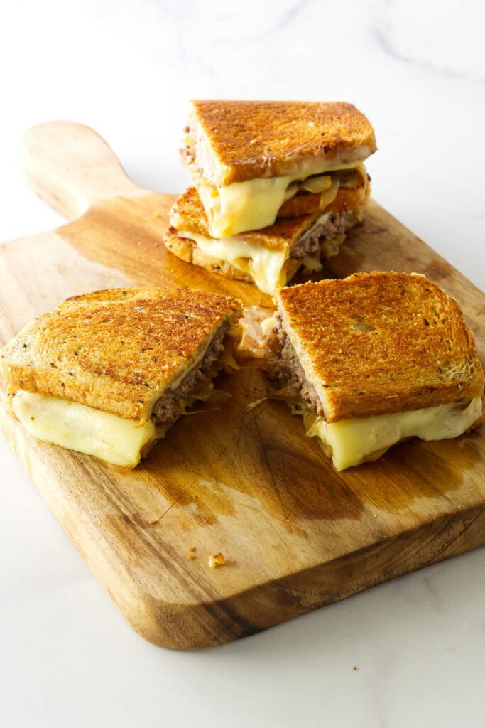 Two sliced patty melt sandwiches on a cutting board.