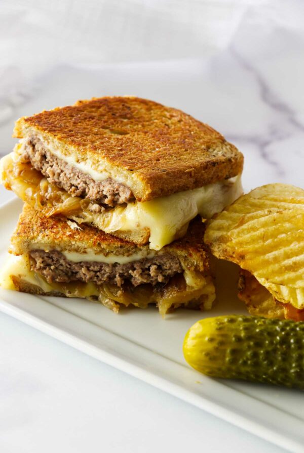 A homemade patty melton a plate with chips and a pickle.