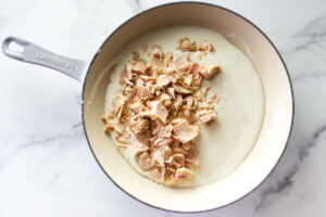 Adding tuna to the creamy mixture in the skillet.
