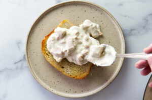 Spooning creamed tuna on a piece of toast.