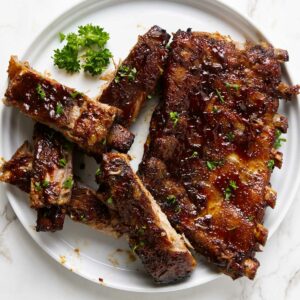 Ribs sliced apart on a white plate, covered in bbq sauce.