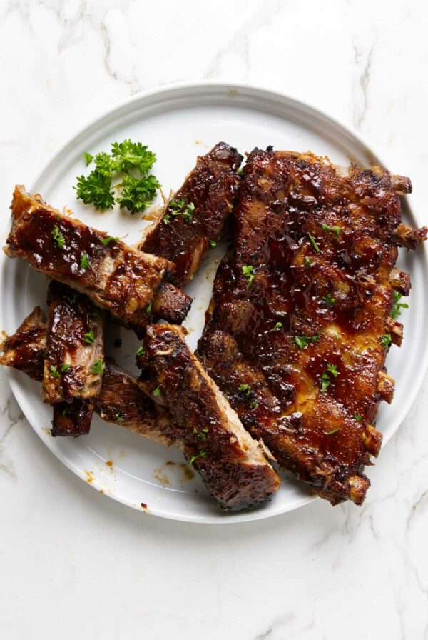 Ribs sliced apart on a white plate, covered in bbq sauce.