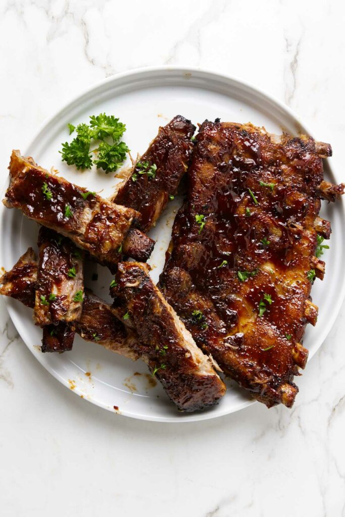 Ribs sliced apart on a white plate, covered in bbq sauce.