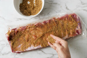 Adding a brown sugar spice rub to pork ribs.