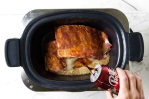 Pouring dr. pepper in a slow cooker with ribs.