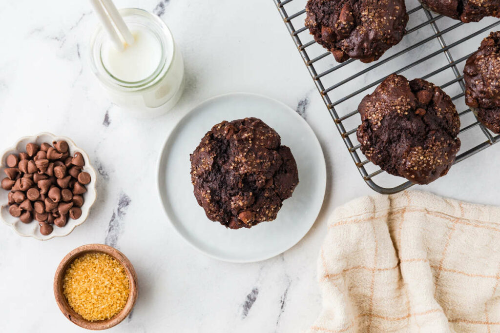 A discard chocolate muffin on a plate next to chocolate chips and milk.