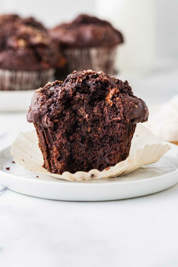 A chocolate sourdough muffin on a plate with muffins in the back.