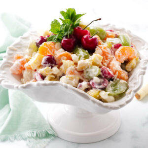 An ambrosia salad made with fresh fruit and three cherries on top.