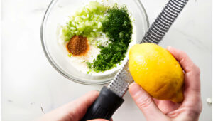 Mixing lemon zest into a bowl with mayo and herbs.