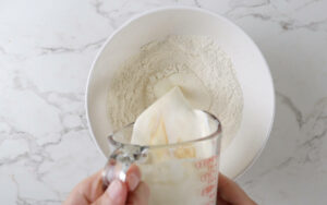Pouring cold cream and vanilla into a bowl with the dry ingredients.