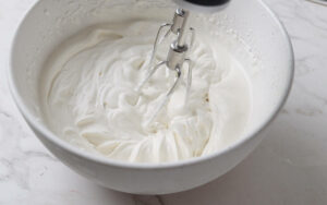 Whipping cream in a bowl with sugar and vanilla extract.