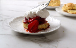 Layering a shortcake biscuit with macerated strawberries and homemade whipped cream.