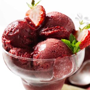 Strawberries and a mint sprig in a dish of strawberry sorbet.