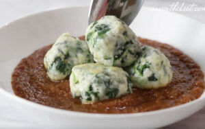Placing spinach ricotta dumplings in tomato sauce.