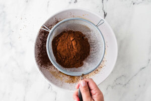 Sifting cocoa powder into the muffin batter.