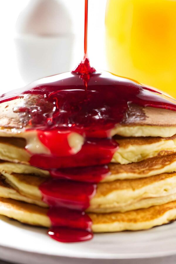 Red syrup drizzling down a stack of ricotta pancakes.