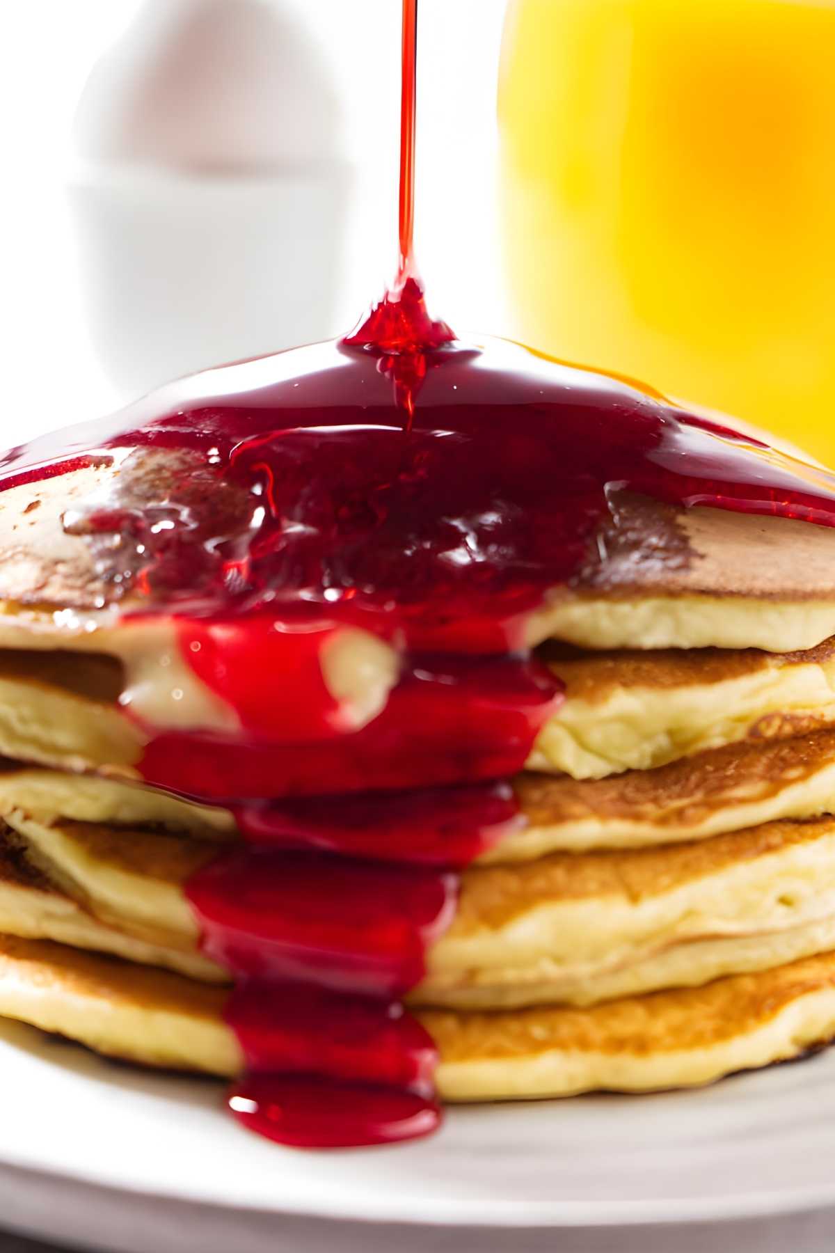 Red syrup drizzling down a stack of ricotta pancakes.