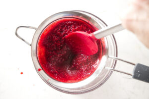 Straining raspberry puree into a bowl.