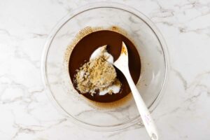 Adding sugar to a mixing bowl with melted chocolate.