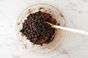 Stirring chocolate chips into sourdough fudge cookies.