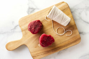 Two beef tenderloin medallions on a cutting board with kitchen string.