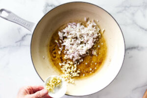 Adding shallots and garlic to a skillet for pan-seared steak.
