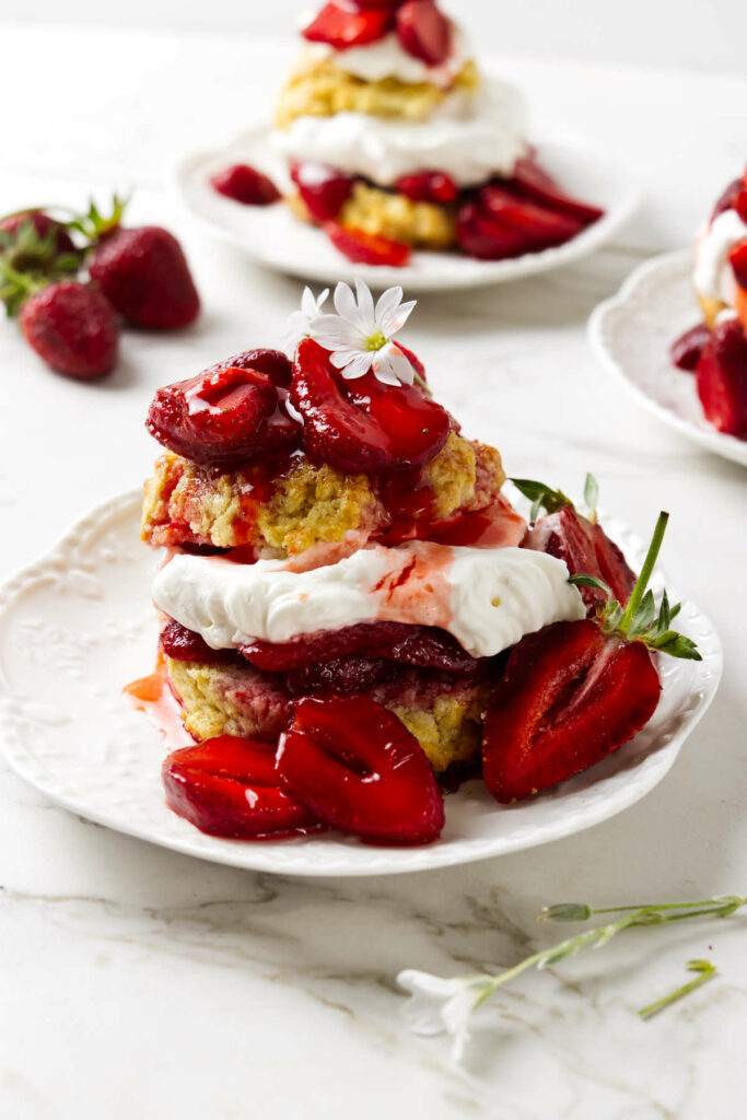 Three individual strawberry shortcake desserts on white plates.