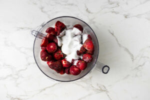 Strawberries and sugar in food processor bowl.