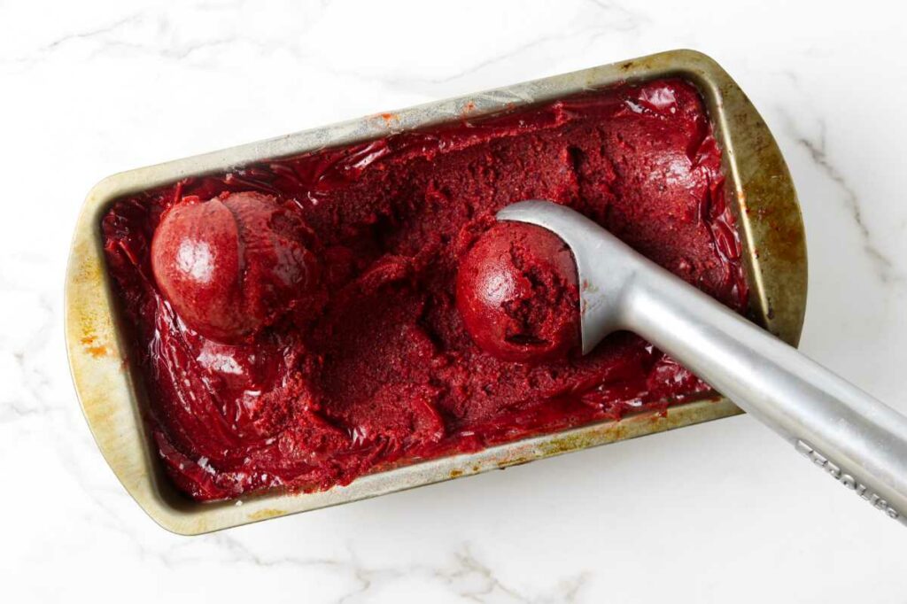 Scooping strawberry sorbet out of a loaf pan.