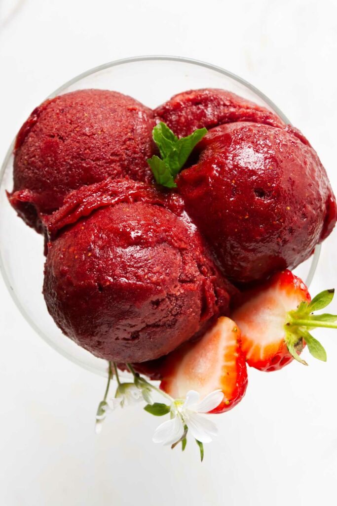 Three scoops of homemade strawberry sorbet in a glass.