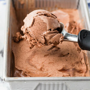 An ice cream scooper with chocolate ice cream.