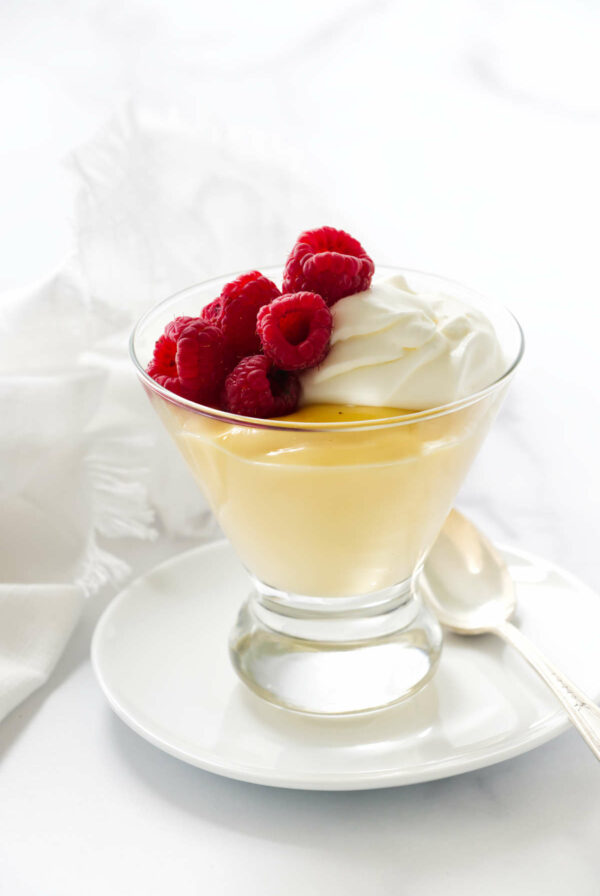 A vanilla pudding recipe from scratch in a glass with raspberries on top.