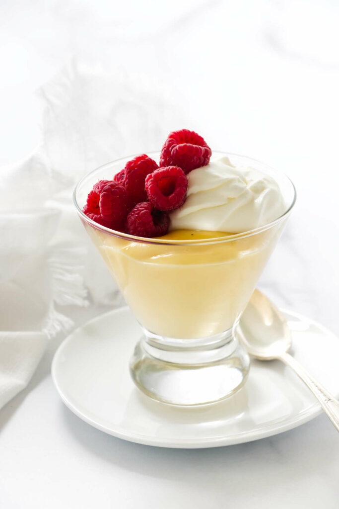 A vanilla pudding recipe from scratch in a glass with raspberries on top.