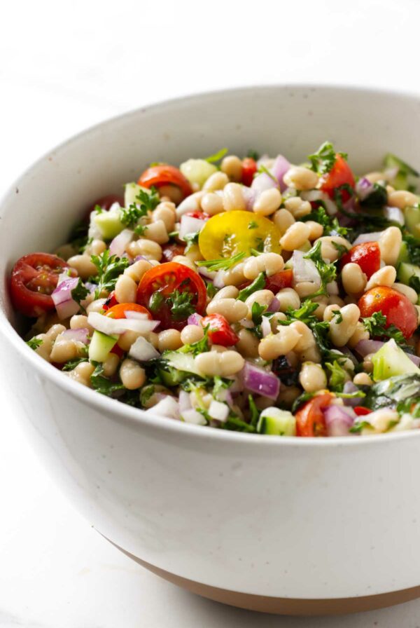 A bean salad with tomatoes and parsley in a bowl.
